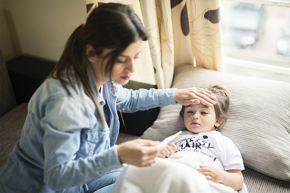 A mother looks after her sick child lying in bed, taking their temperature and checking for symptoms of hand-foot-and-mouth disease.