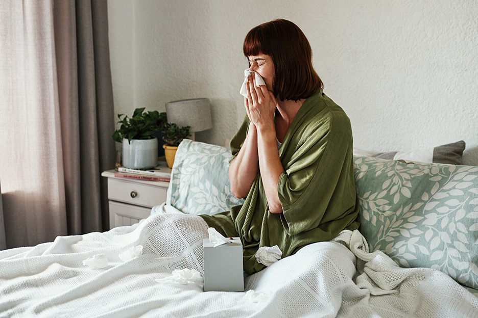 Woman with sinusitis blowing her nose while sitting in bed.